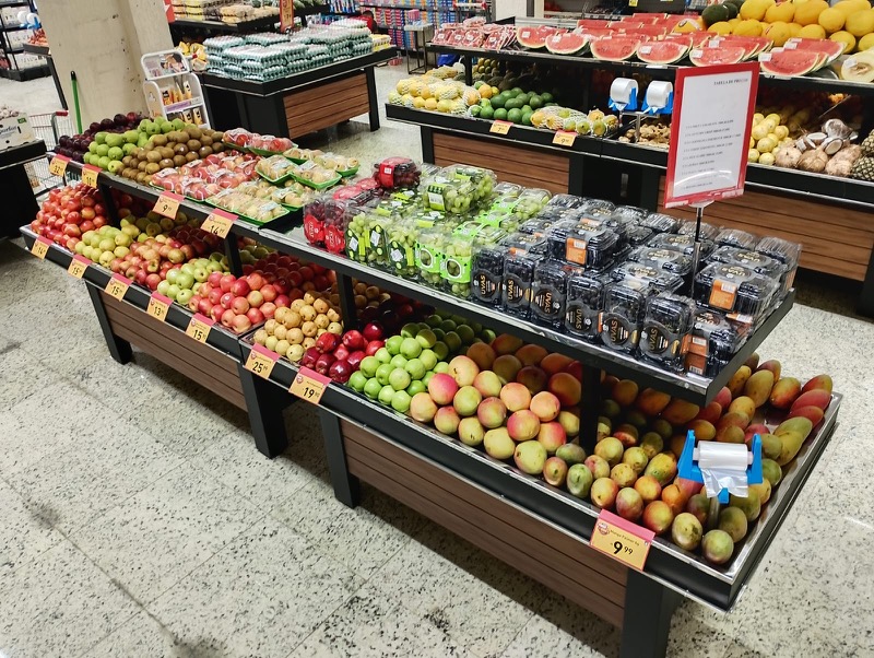 Banca de centro com maçãs, uvas e mangas em dois níveis de exposição.