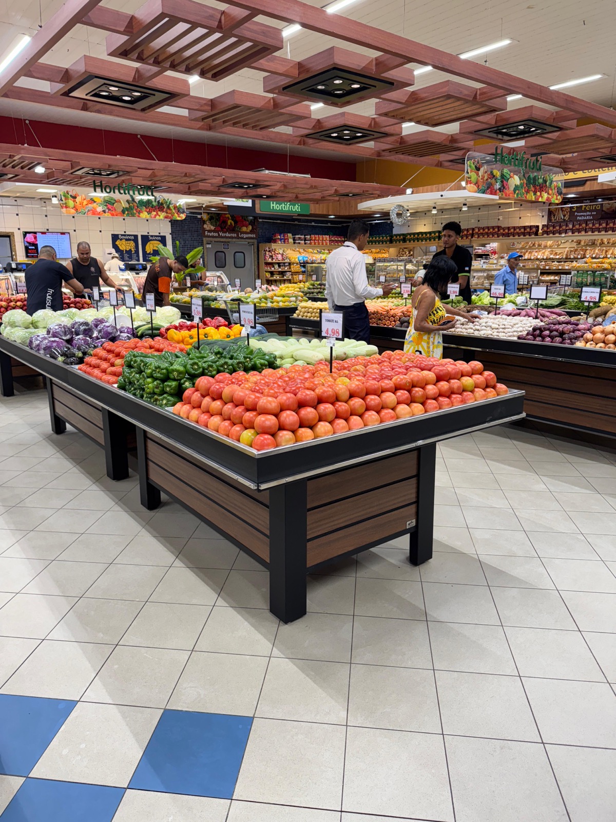 Banca de centro da Metalúrgica Rios instalada no setor de hortifruti de um supermercado, carregada de tomates, pimentões e verduras.